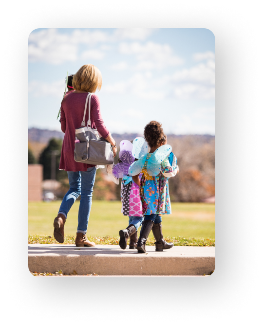 woman walking with two children and carrying one