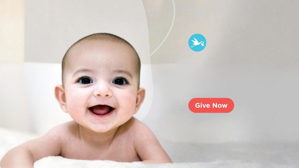 Baby on white carpet smiling at camera. Give Now
