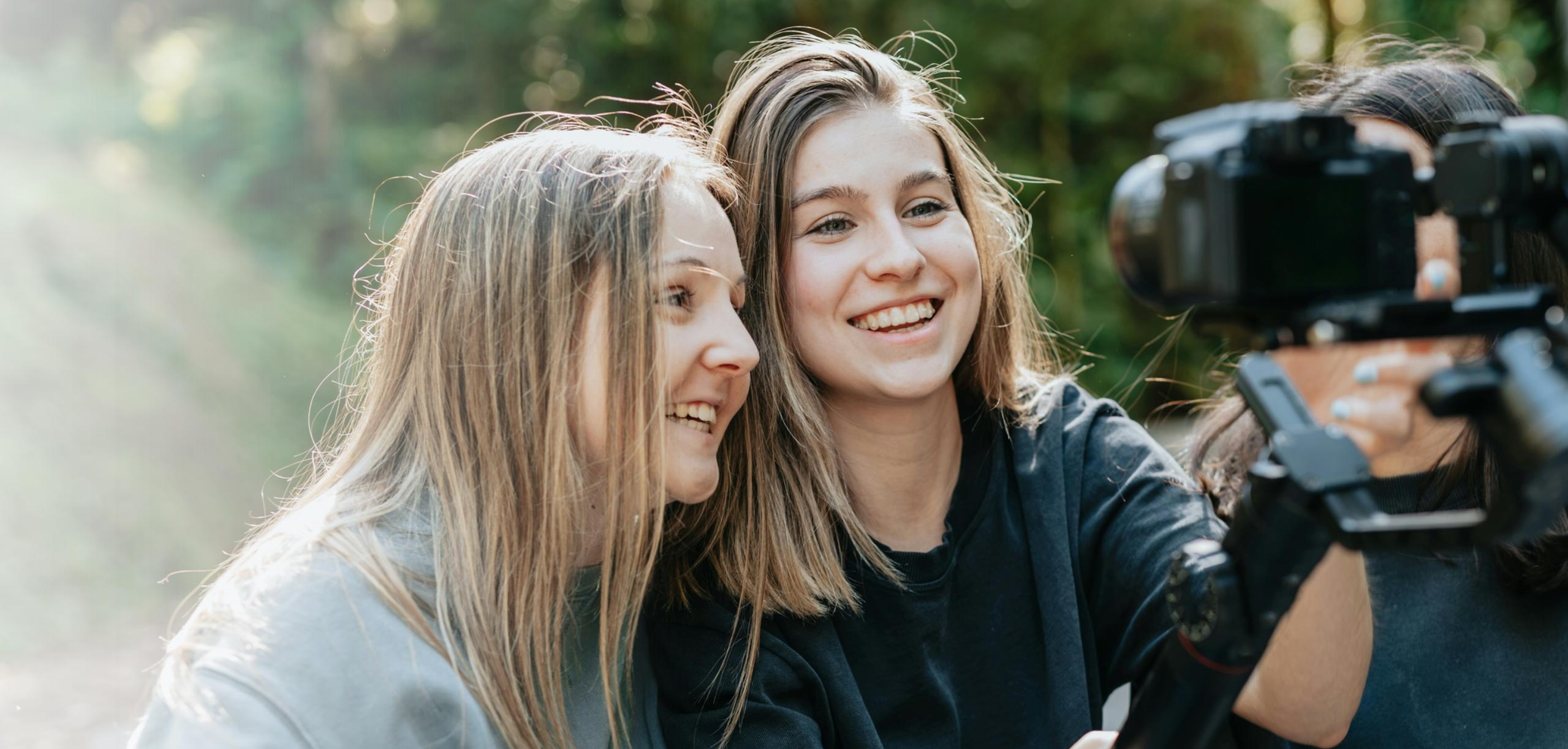 Two women smiling and taking a picture of themselves with a DSLR camera.
